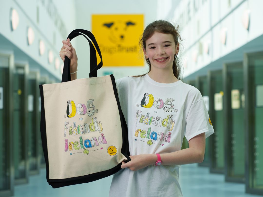 12-year-old Aishling wearing a t-shirt with a 'dog friendly Ireland' print holds up a tote bag with the same design in the Rehoming Corridor.