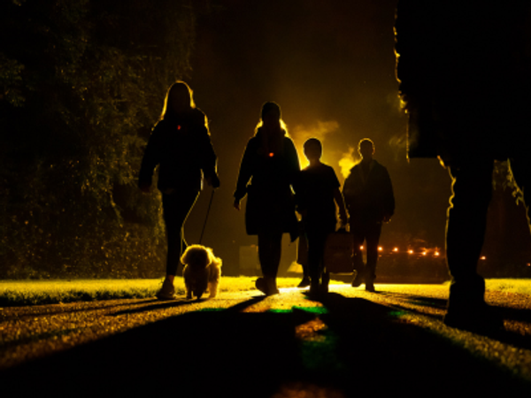 Photo of a family walking with their small dog in the dark. The family are lit up from behind by a bright yellow light