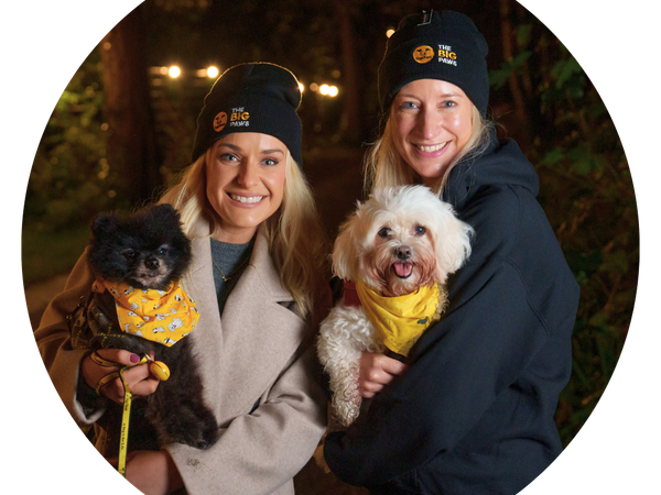 Two women holding dogs smile at the camera at the Big Paws memorial walk