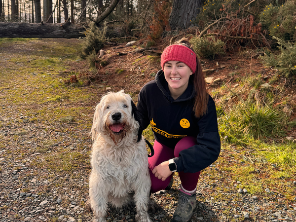 Woman kneeling next to dog in a forest