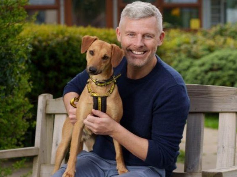 Smiling man sat on a bench holding a dog